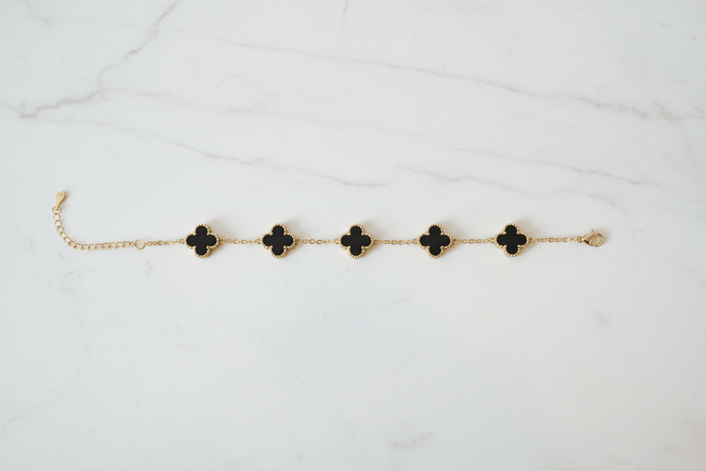 Gold black clover charm bracelet on white marble surface