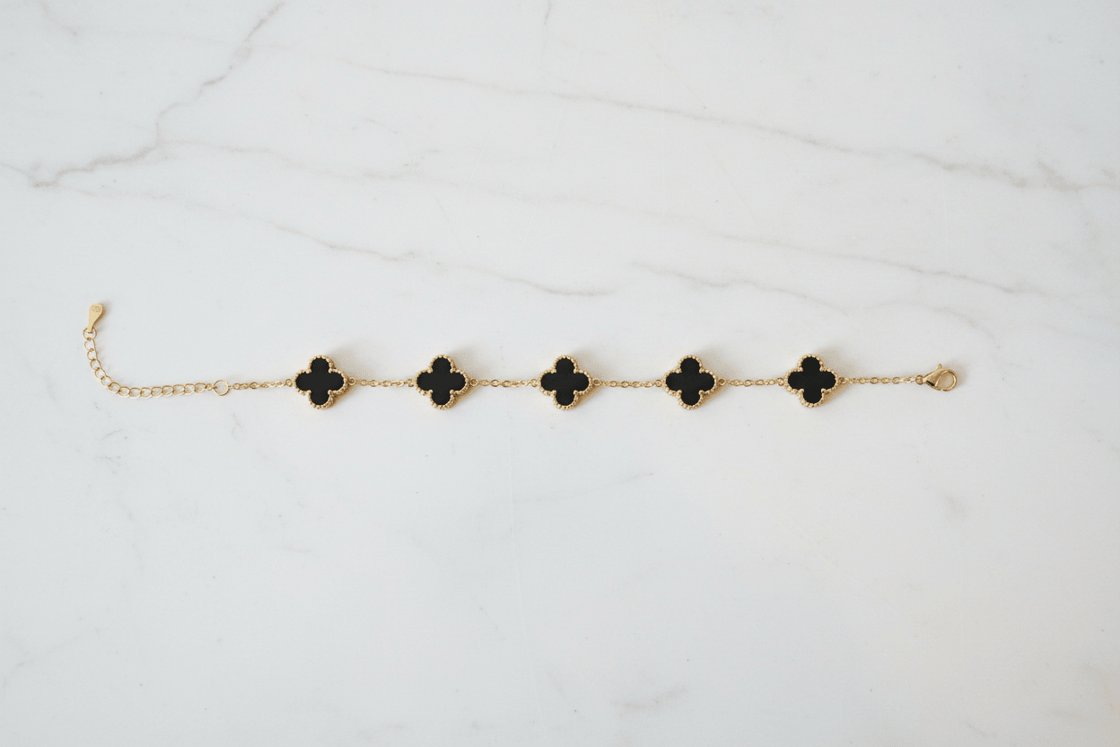 Gold black clover charm bracelet on white marble surface