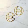 Gold CC hoop earrings on white marble surface