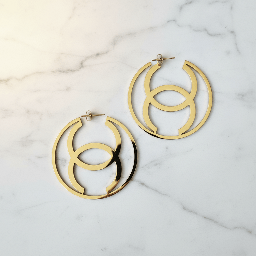 Gold CC hoop earrings on white marble surface