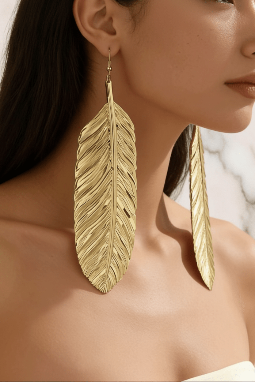 Oversized Gold Feather Drop Earrings worn by brown skin model on marble background